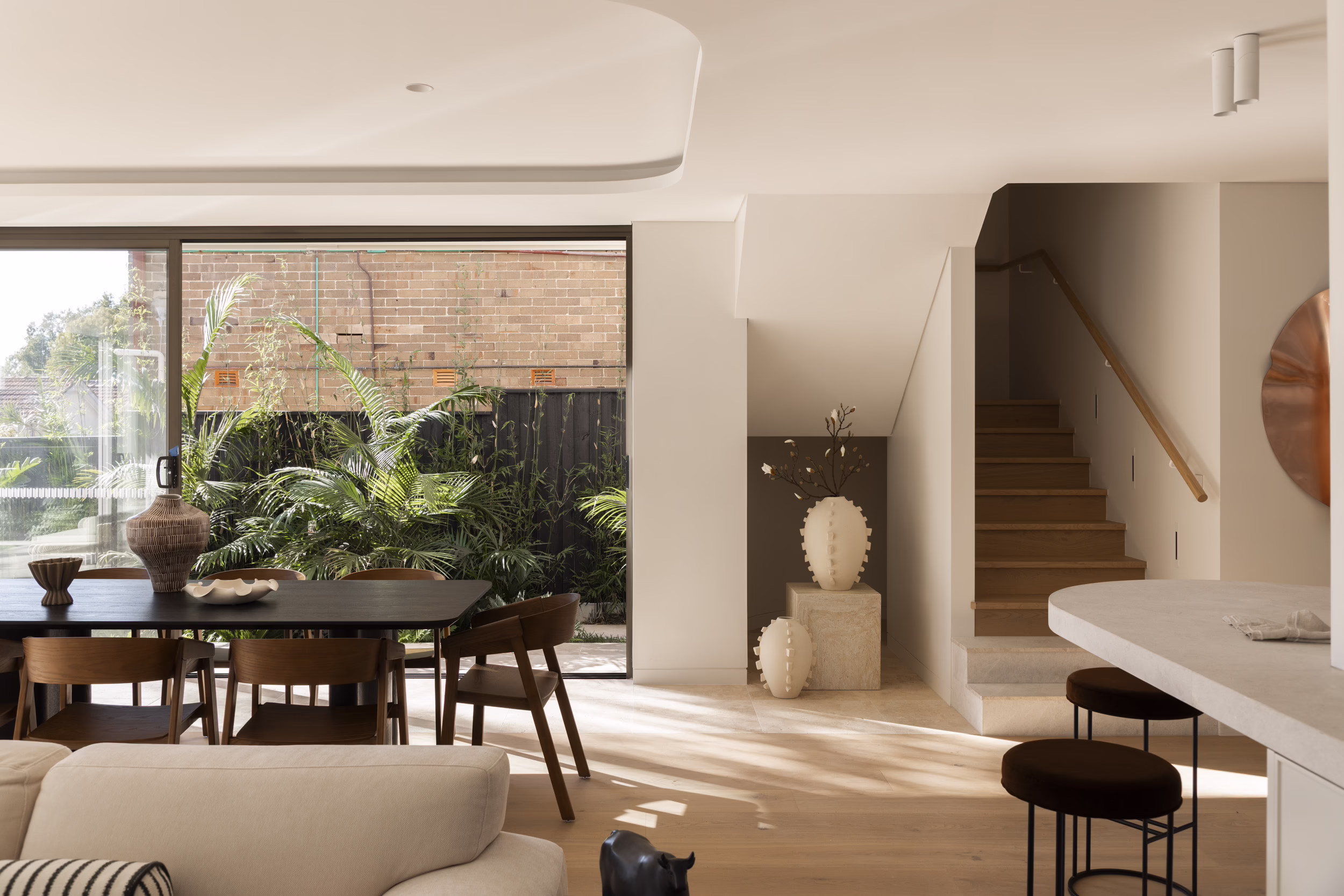 Open-plan dining and kitchen area at Edward Street House, beside a timber staircase and planted side garden