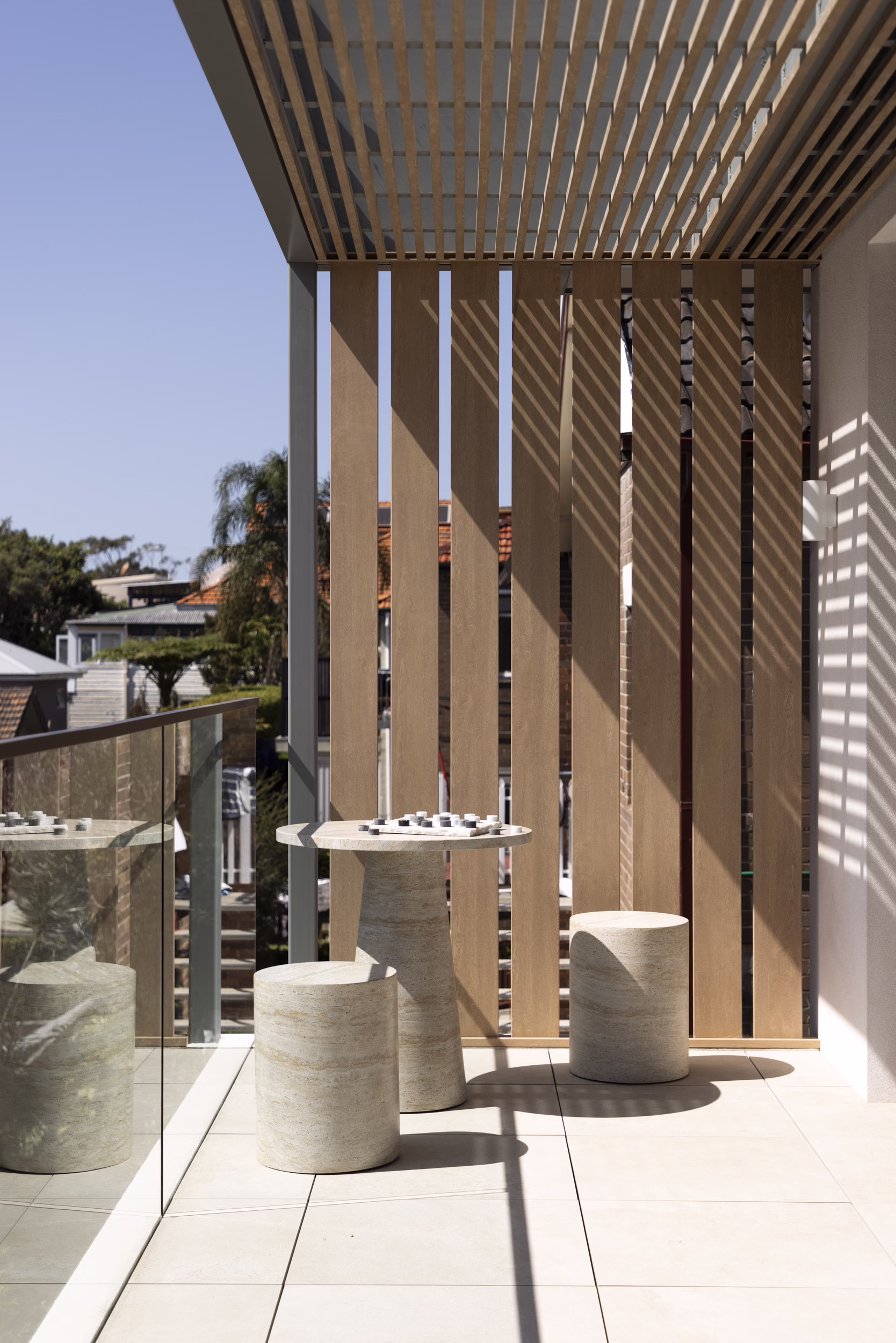 Sunlit balcony at Edward Street House with vertical screening, slatted shade canopy and a small table with stools